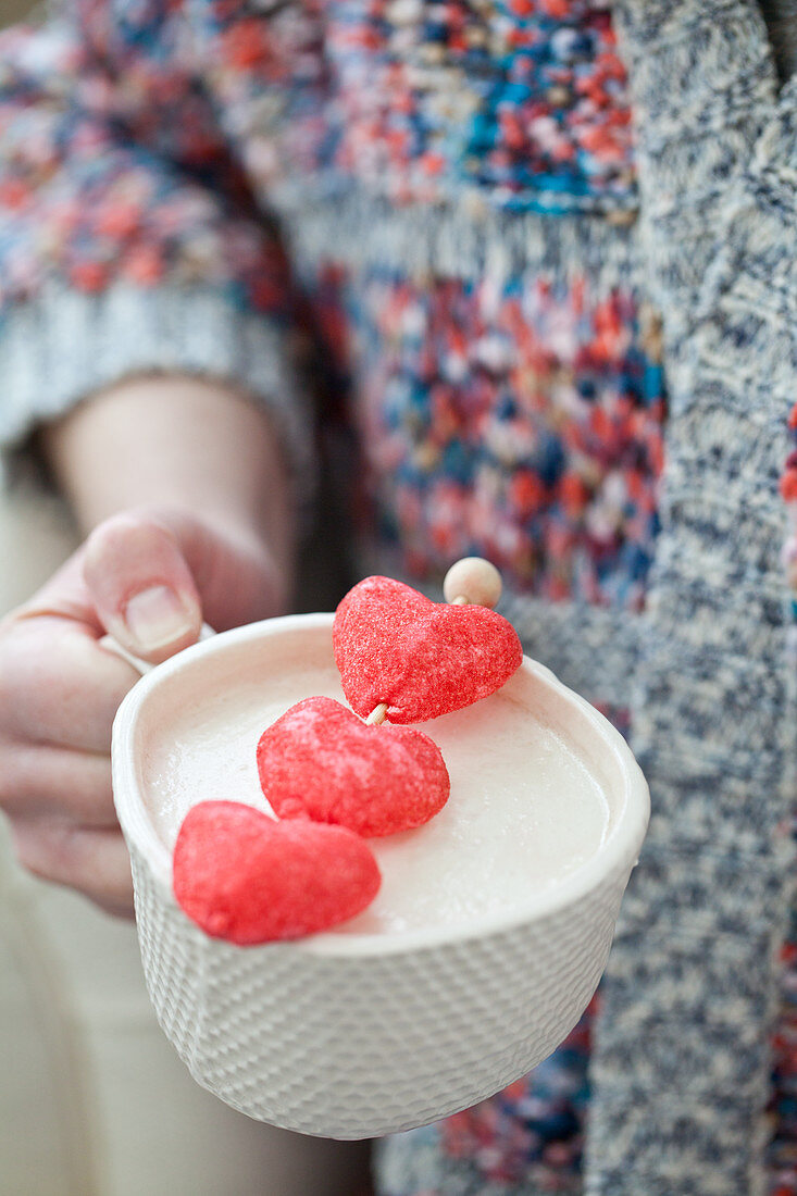 Weiße heiße Schokolade in Tasse dekoriert mit herzförmigen roten Marshmallows
