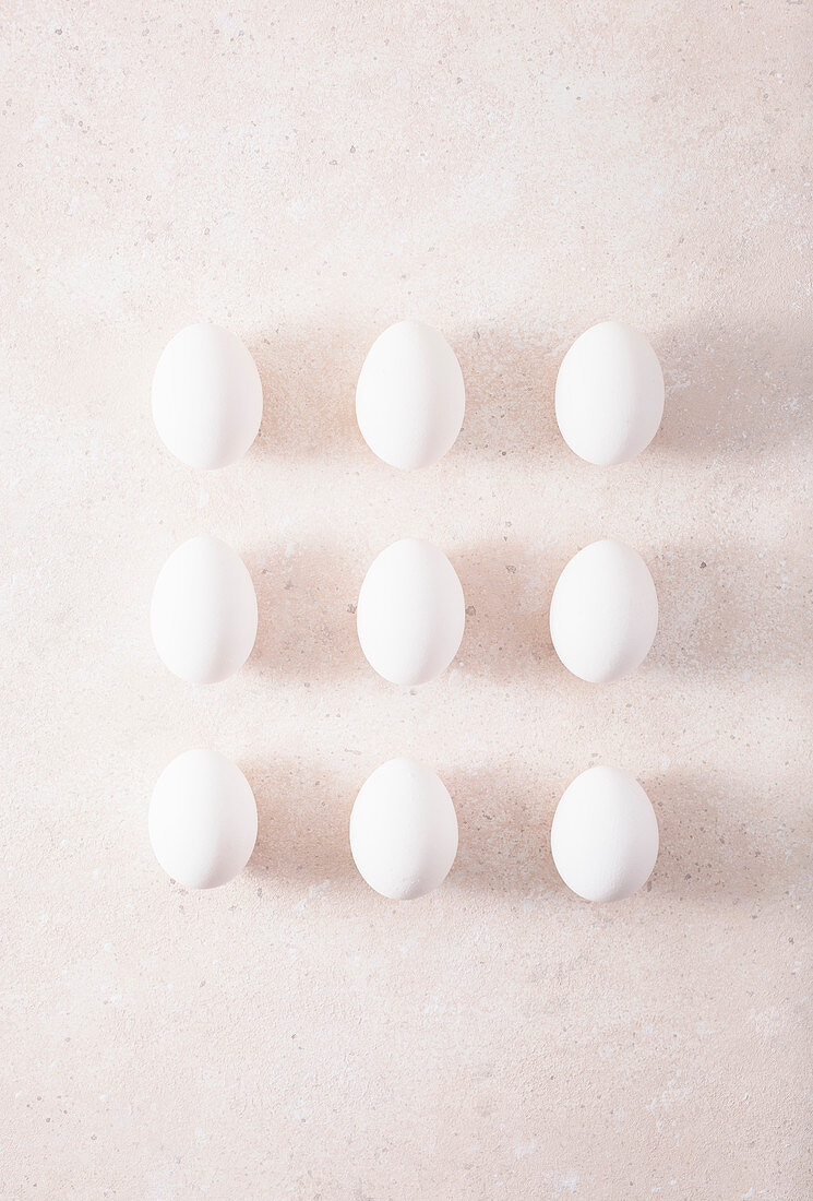 Nine white hen's eggs in rows on a light surface