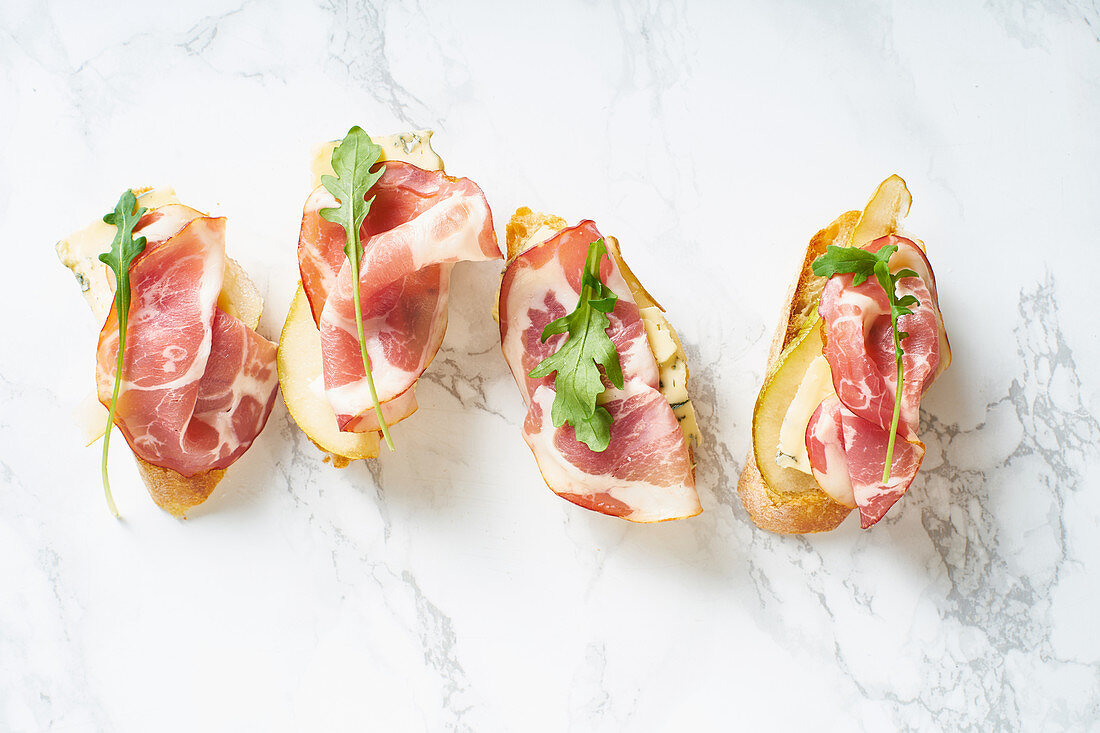 A set of bruschettas with cured meat, pear, blue cheese and ruccola