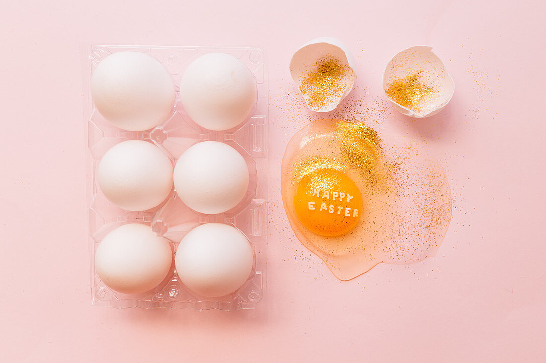 Osterstilleben mit aufgeschlagenem Ei, Eierschalen und Goldglitter
