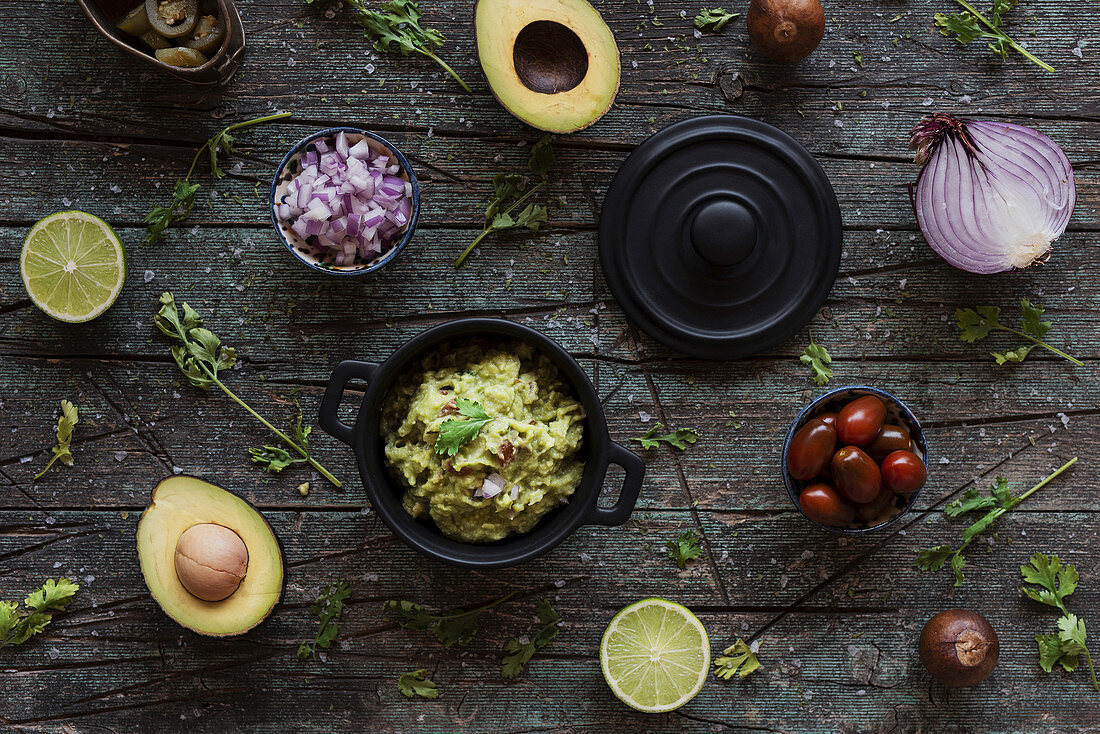 Various fresh ingredients placed on lumber table near pot with yummy guacamole