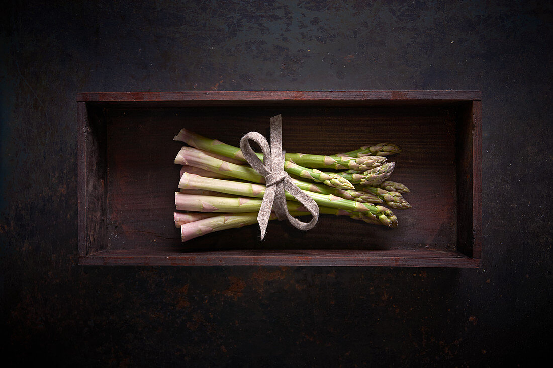 A bundle of fresh green asparagus in a wooden box on a dark surface
