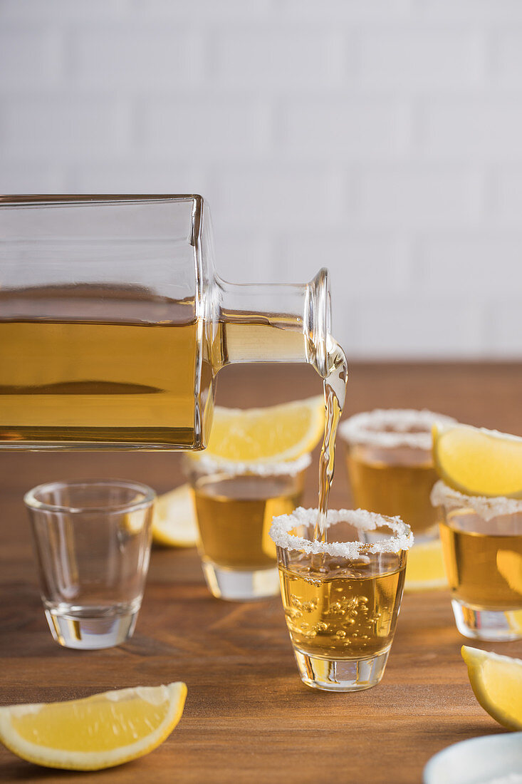 Glass shots of golden tequila with salty rim and slices of lemon on top