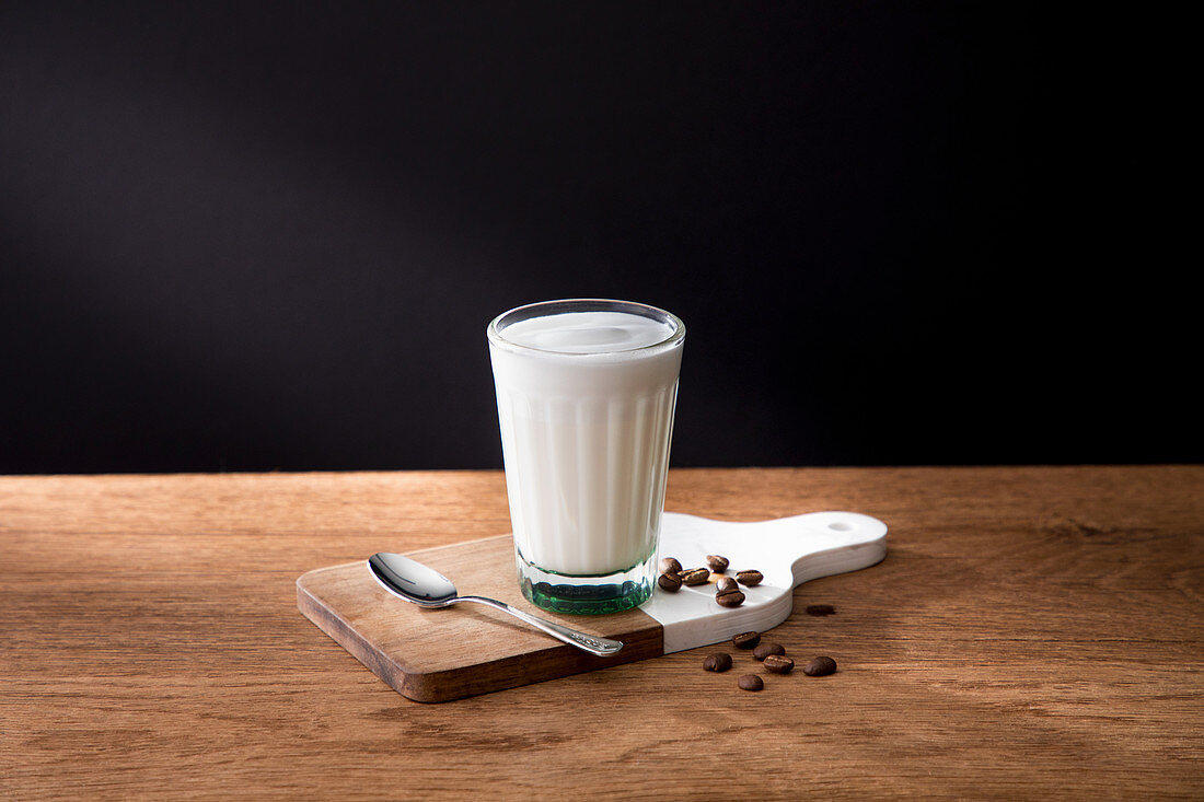 Glass of fresh milk on wooden board with spoon and coffee grains