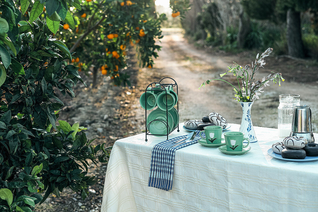 Gartentisch mit Kaffeetassen, süssem Gebäck und Kaffeekanne