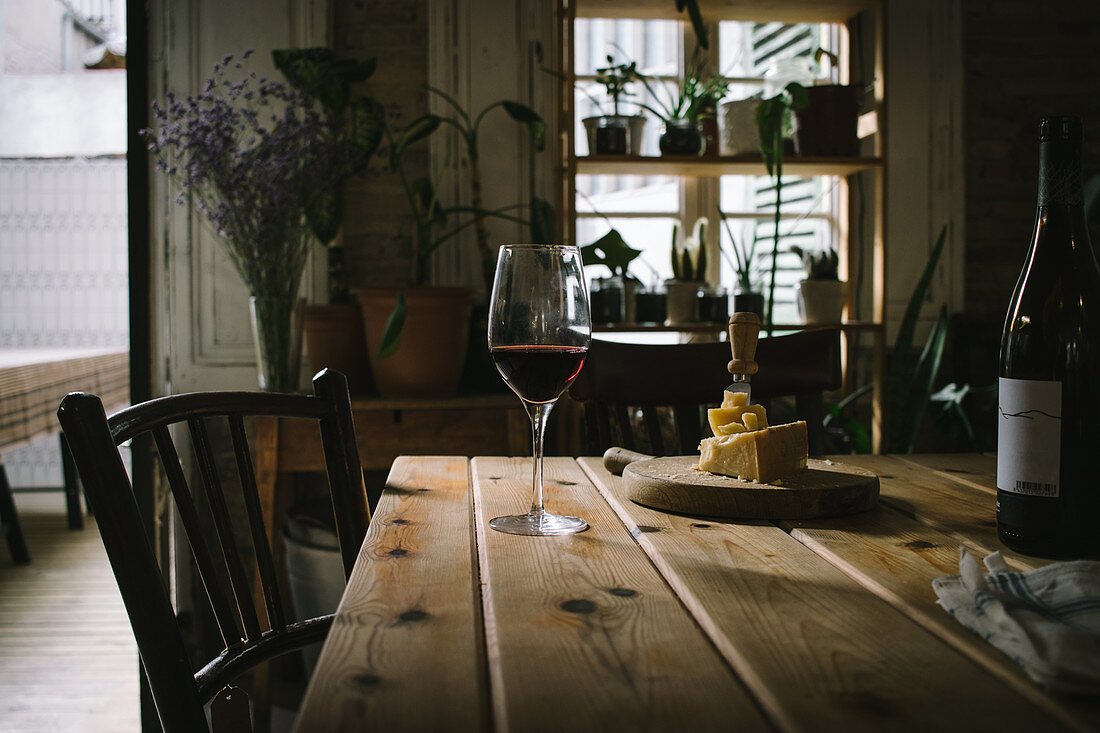 Bottle and glass of red wine and cheeseboard on rustic wooden table