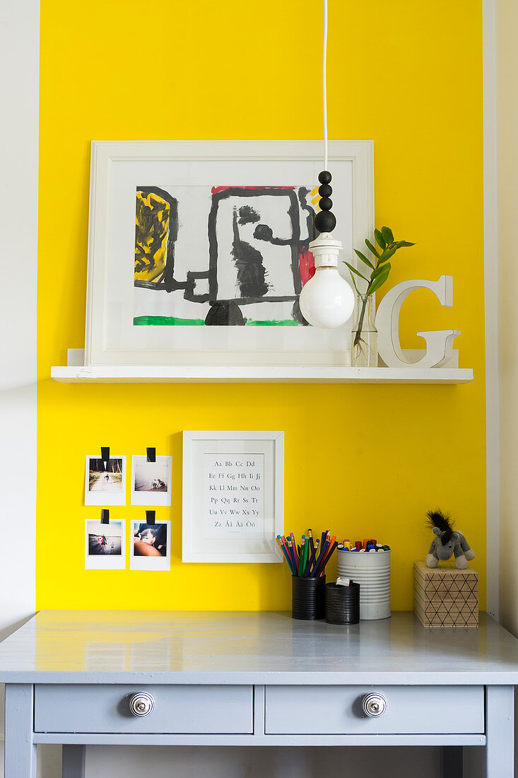 Shelf on yellow wall above grey desk