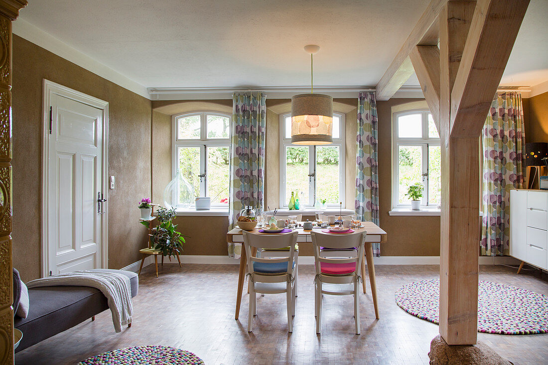 Dining area in front of windows in open-plan interior with wooden pillars