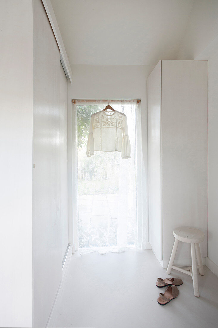 Pretty blouse hanging in window with airy curtains in white interior
