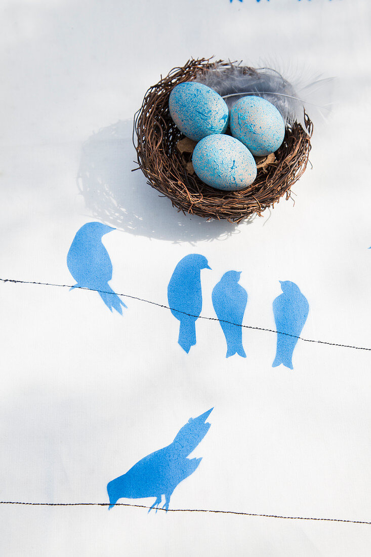 Blue-dyed eggs in Easter nest on tablecloth with stencilled bird motif
