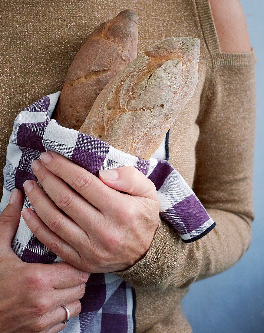 A woman holding baguettes wrapped in a cloth