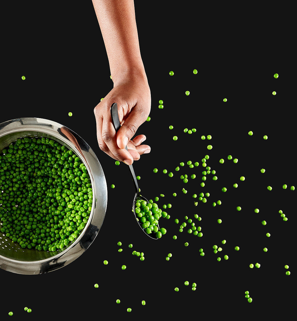 A hand spoons peas out of a metal colander