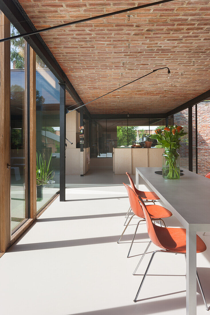 Heller Wohnraum mit Glasfront, Ziegeldecke und orangefarbenen Stühlen