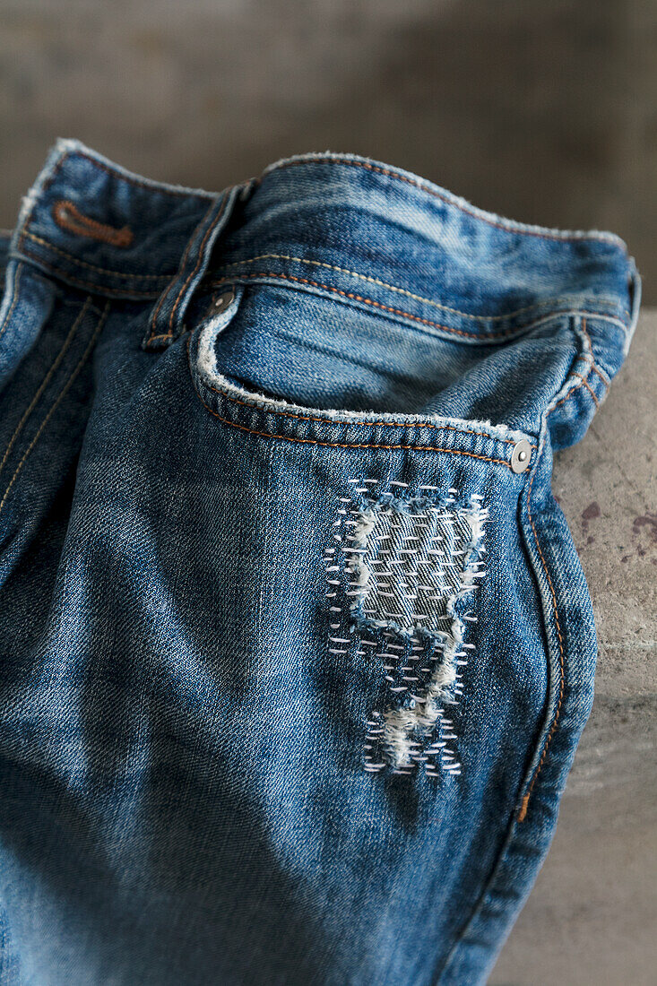 Seam detail of repaired blue jeans on concrete background