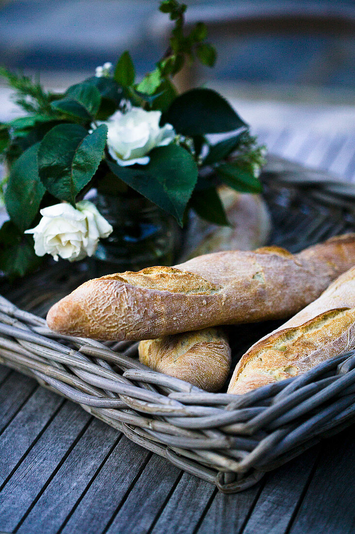 Korbtablett mit Baguettes und Blumen auf Holztisch