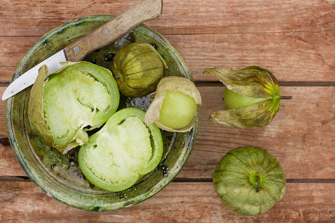 Green tomatillos in a ceramic bowl with a knife