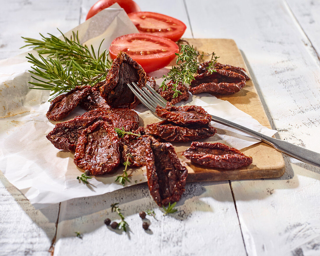 Tomaten, getrocknet und frisch, mit Thymian und Rosmarin auf Schneidebrett