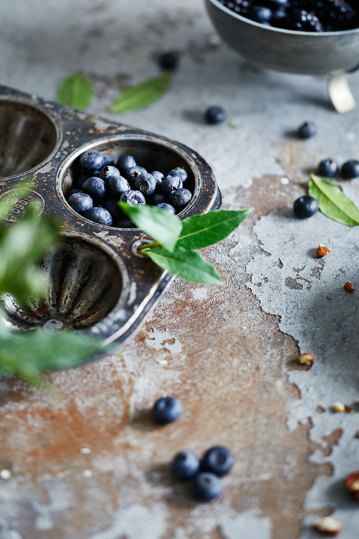 Blueberries and bay leaves in a muffin tray on a rustic surface