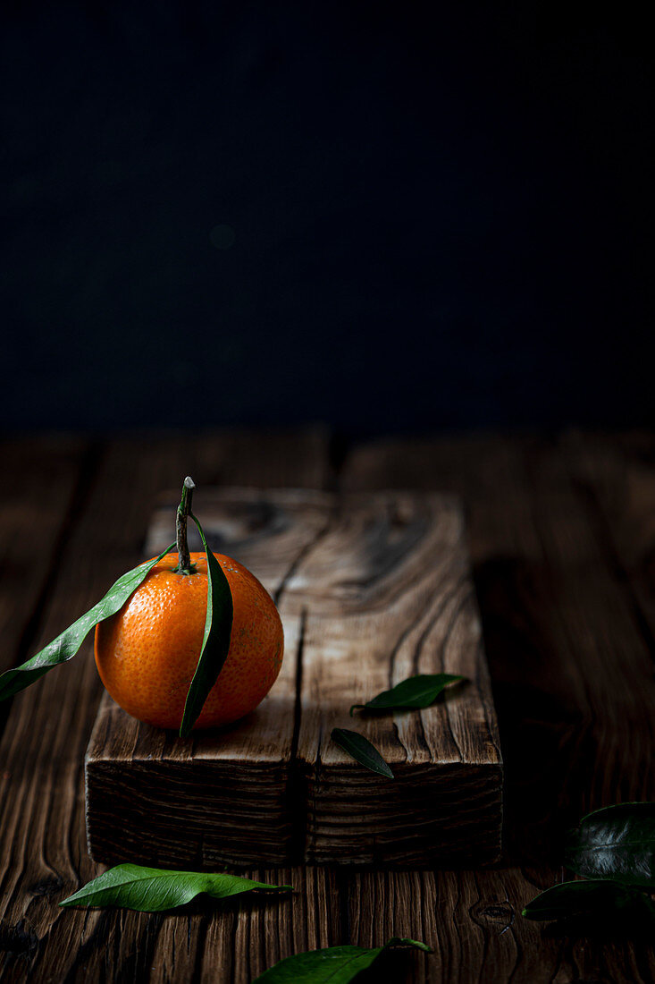 Clementine mit Blättern auf Holzbrett vor dunklem Hintergrund
