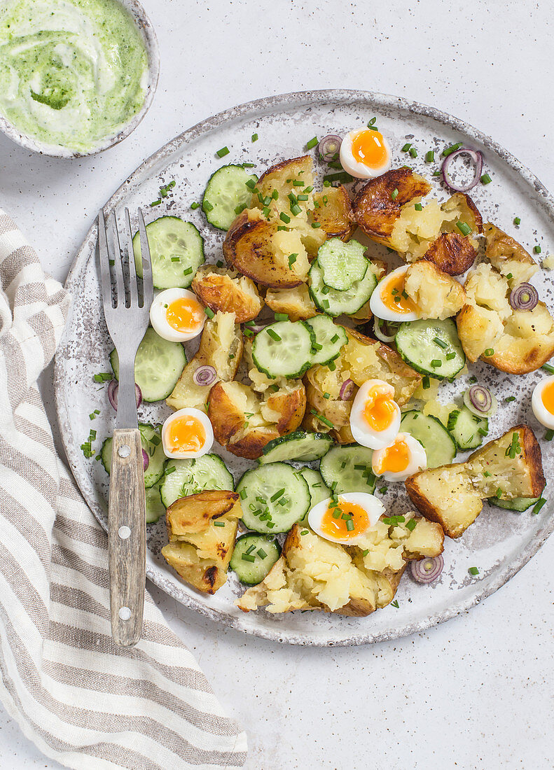 Roasted potato, cucumber and quail eggs salad, served on grey plate with green dressing