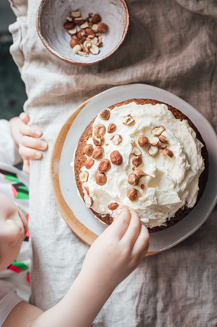 Kleines Mädchen verziert Karottenkuchen mit Haselnüssen