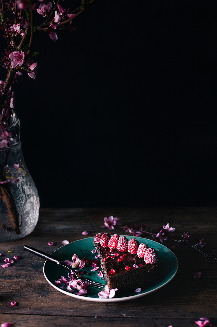 Ein Stück Mohnkuchen dekoriert mit gefrosteten Himbeeren und rosa Blüten