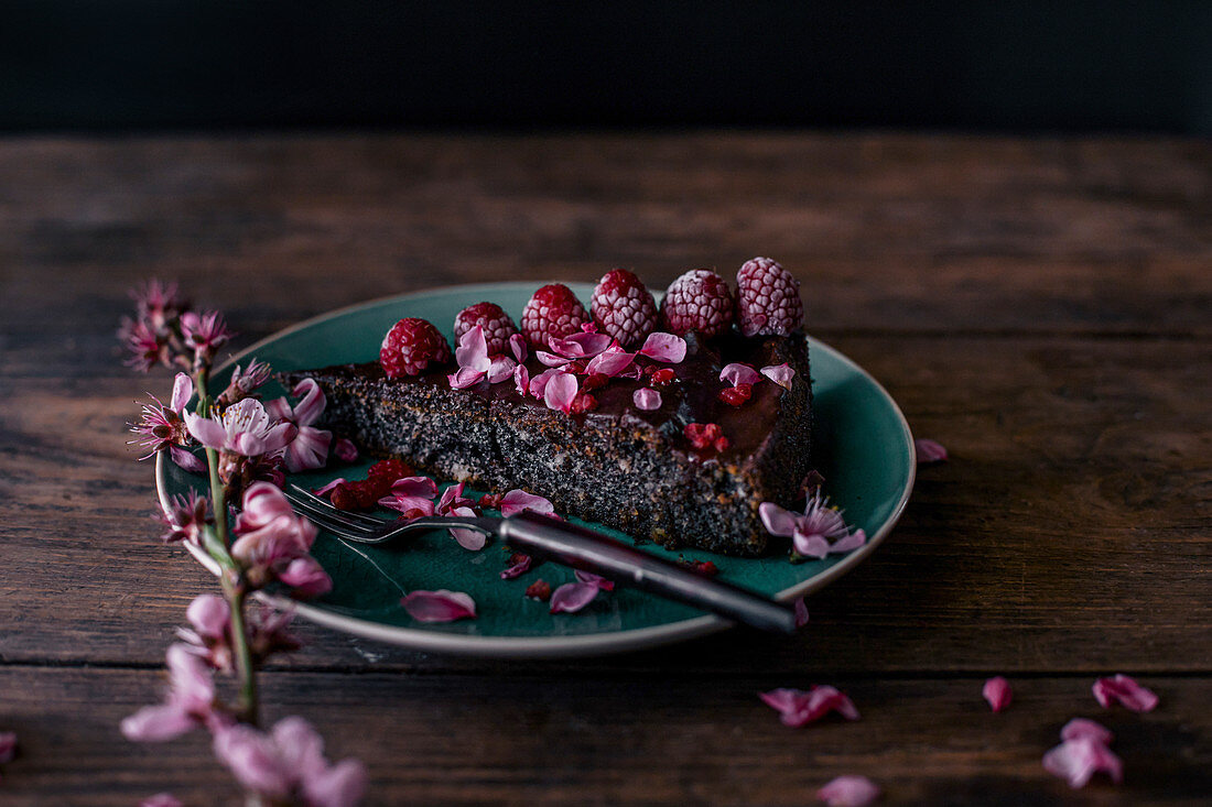 Ein Stück Mohnkuchen dekoriert mit gefrosteten Himbeeren und rosa Blüten