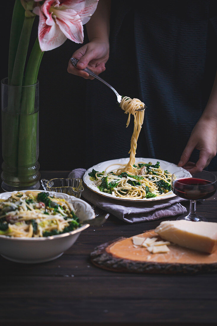 Woman eating spaghetti with kale, green peas, panceta and Parmesan cheese