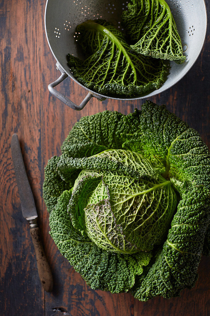 Whole cabbage, and savoy cabbage leaves in a vintage colander