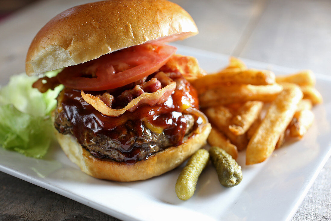 Juicy bacon cheeseburger deluxe with french fries and cornichon pickles