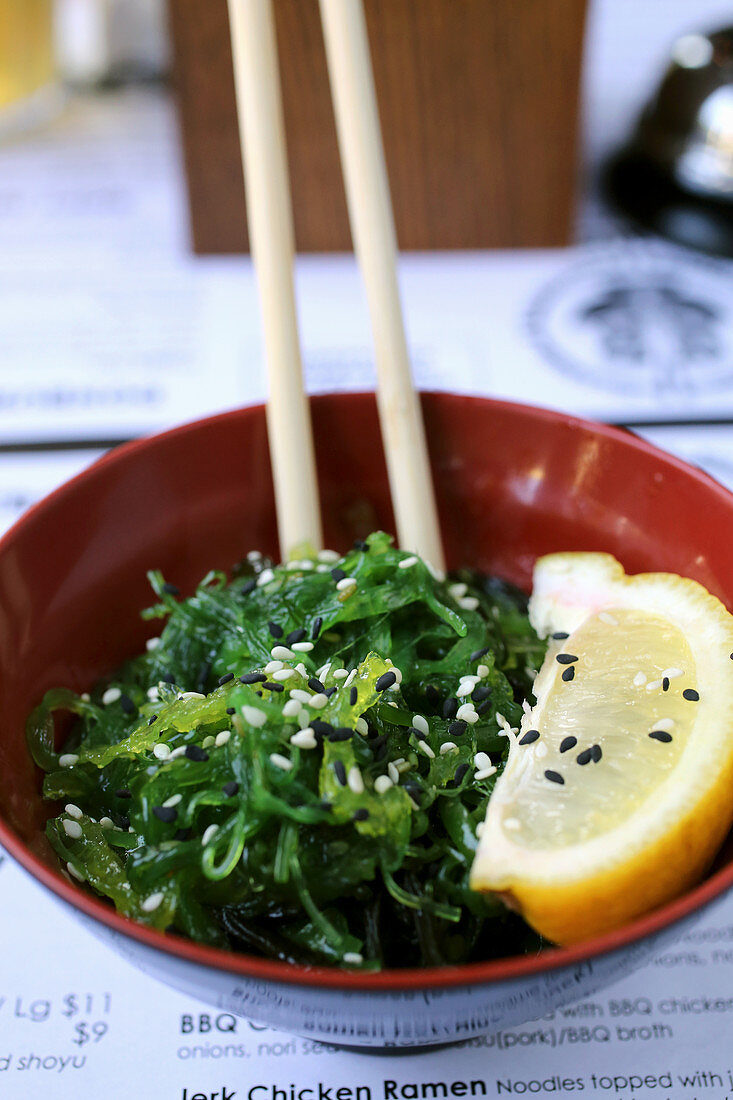 Bowl of seaweed salad topped with sesame seeds and lemon wedge