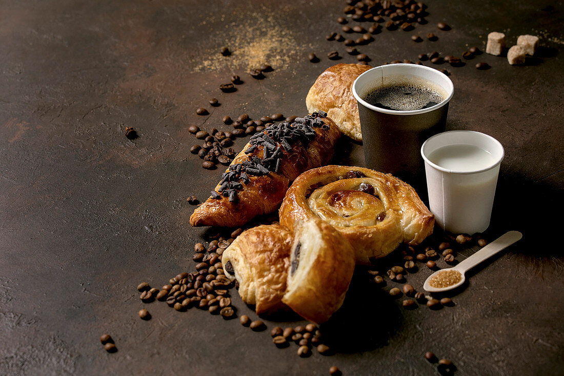 Variety of traditional french puff pastry raisin and chocolate buns, croissant with cups of coffee americano and milk