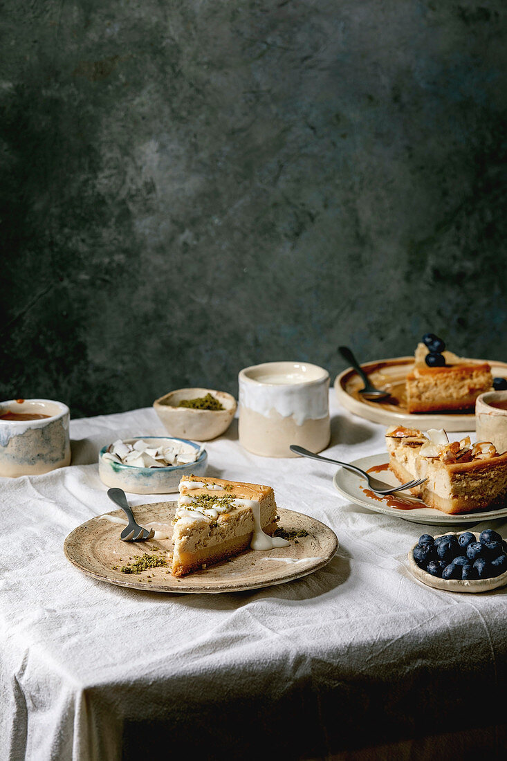 Pieces of cheesecake with different toppings on ceramic plates and variety of sauces in ceramic bowls