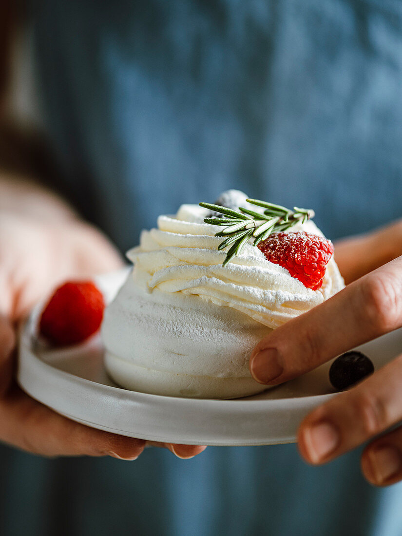 Woman hold plate with mini Pavlova cake decorated fresh berries and rosemary