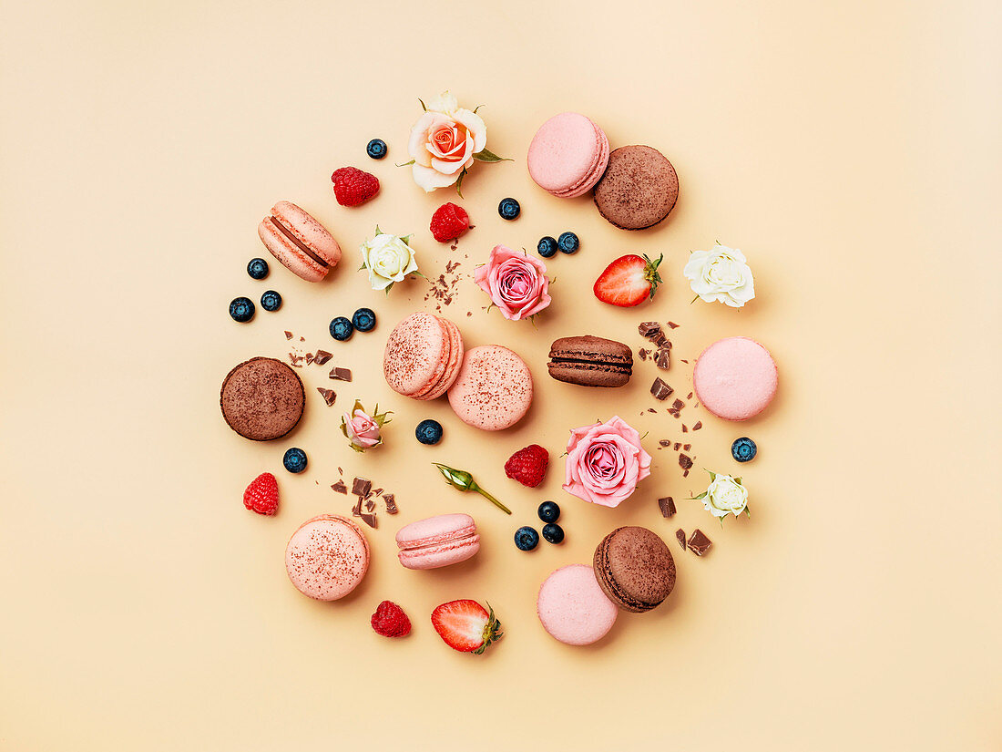 Verschiedene Macarons kreisförmig arrangiert und dekoriert mit Beeren und Rosenblüten