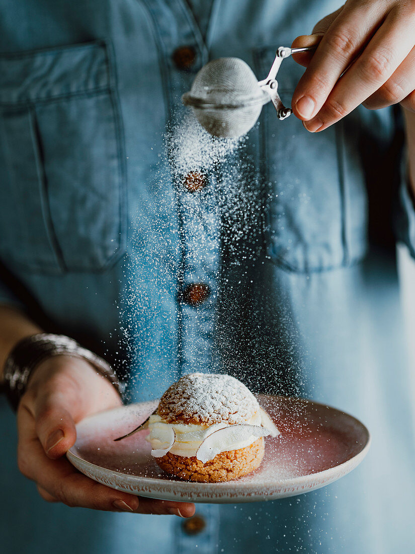 Woman holds with one hand plate with choux au craquelin pastry with icing sugar