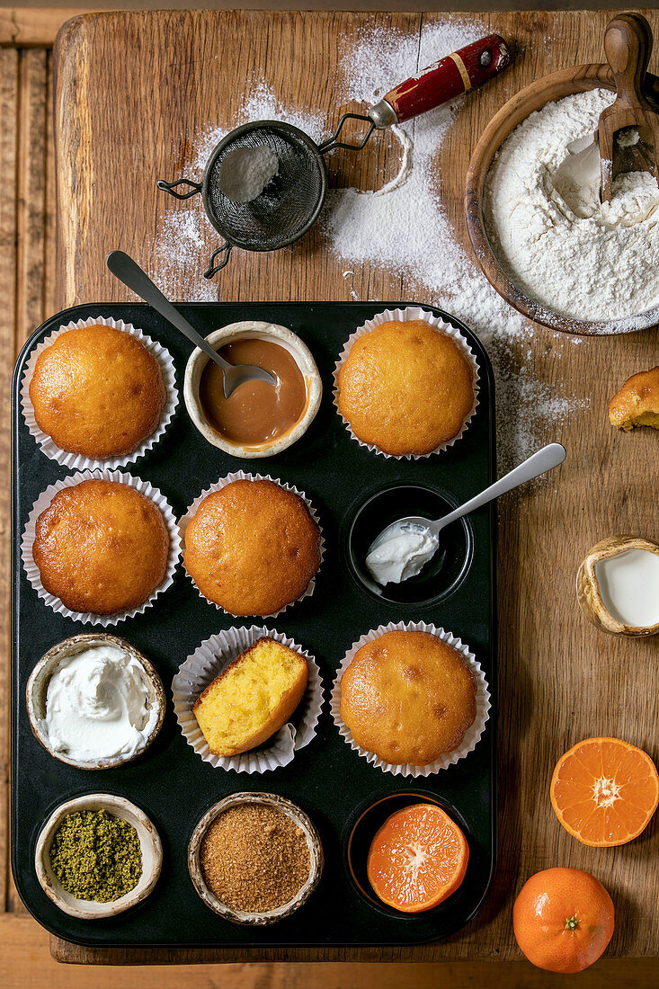 Homemade citrus oranges or clementines sweet muffins cakes in baked tray with flour, ingredients and different topping