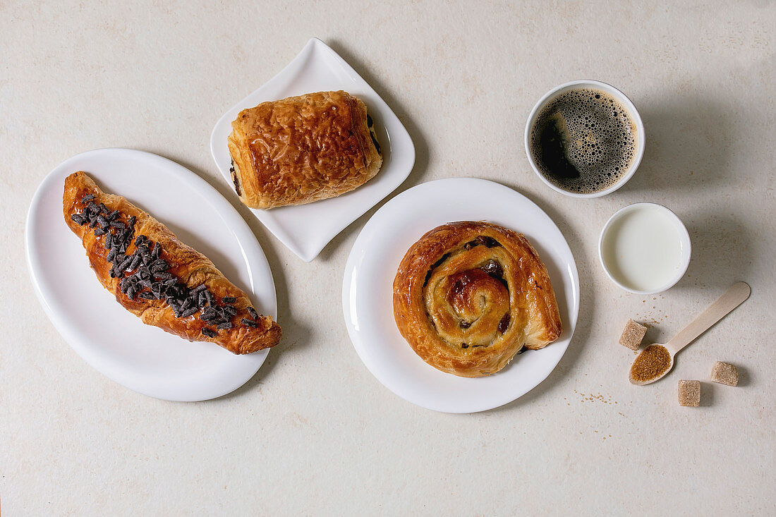 Variety of traditional french puff pastry buns with rasin and chocolate, croissant with paper cup of coffee and milk