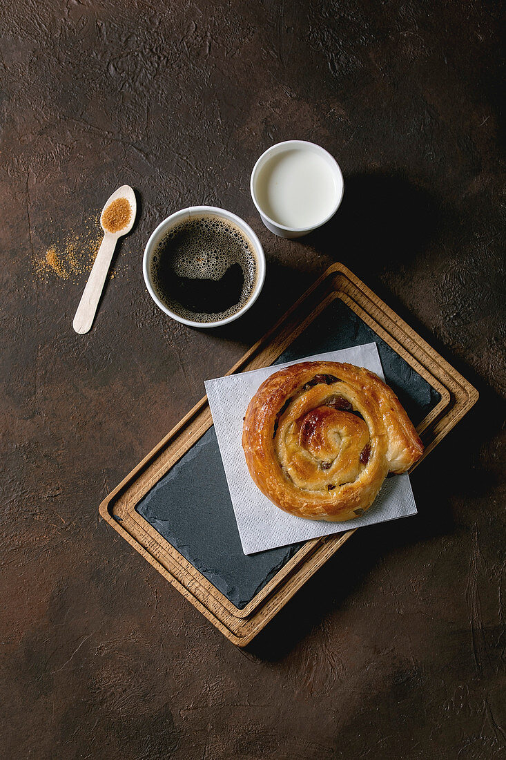 Traditional french puff pastry buns with rasin and custard on slate wooden board with paper cup of coffee and milk