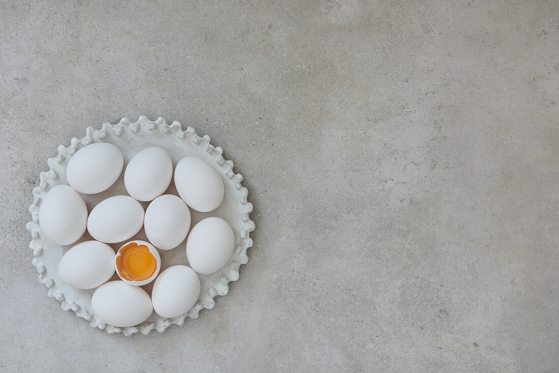 Weisse Eier und aufgeschlagenes Ei auf Keramikteller