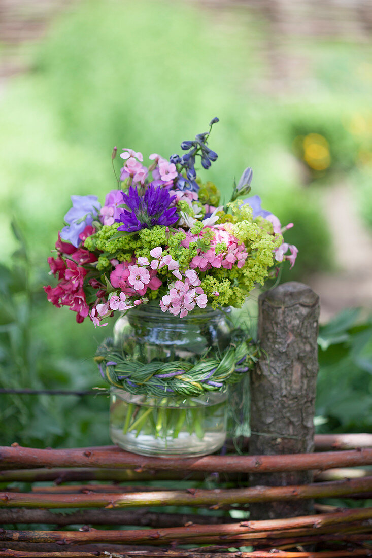 Bouquet in preserving jar with grass braid on top of wattle fence