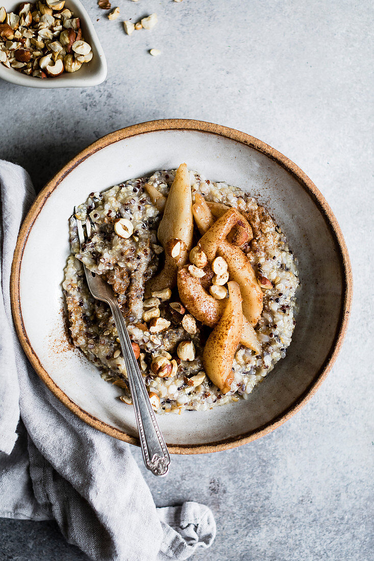 A healthy multigrain porridge with a topping of warm spiced pears and hazelnuts for a hearty breakfast.