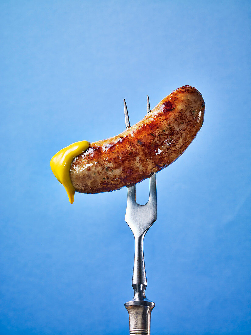 A sausage dipped in mustard on a fork