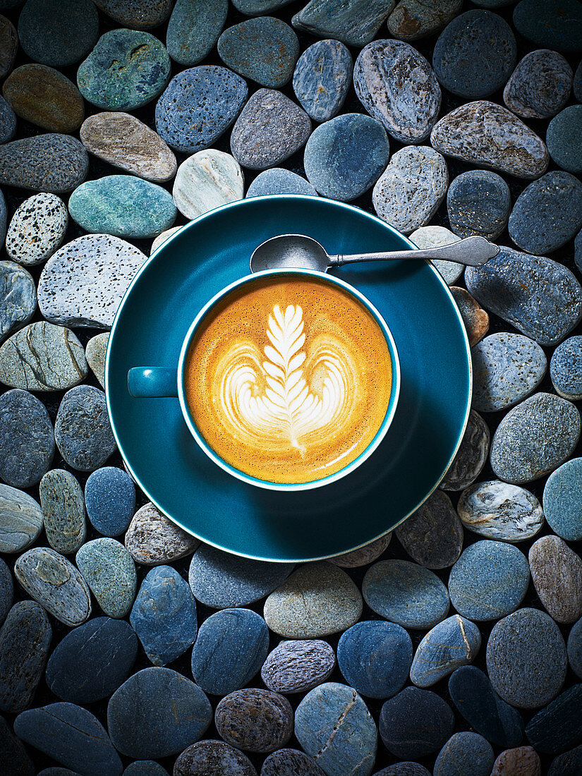 Eine Tasse Kaffee mit Milchschaummotiv auf Kieselstein-Untergrund