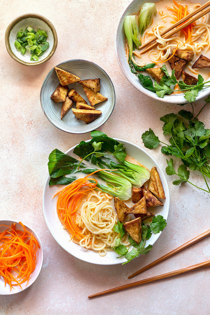 Coconut noodles soup with fried tofu and vegetables on the table.