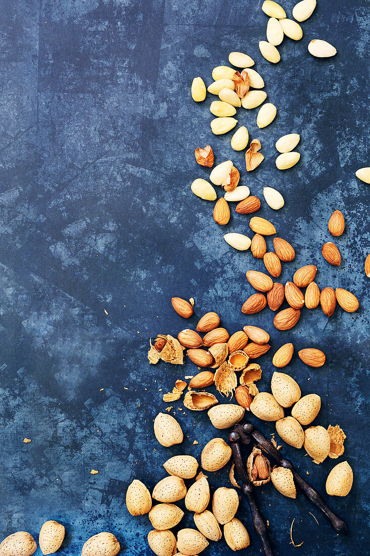 Almonds in shells, almonds kernals and blanched almonds scattered on a textured blue background.