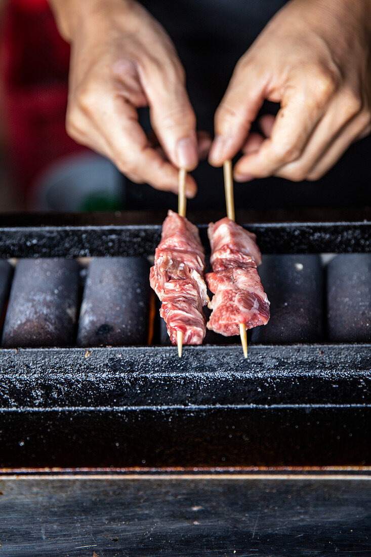 Hands holding skewers on japanese grill