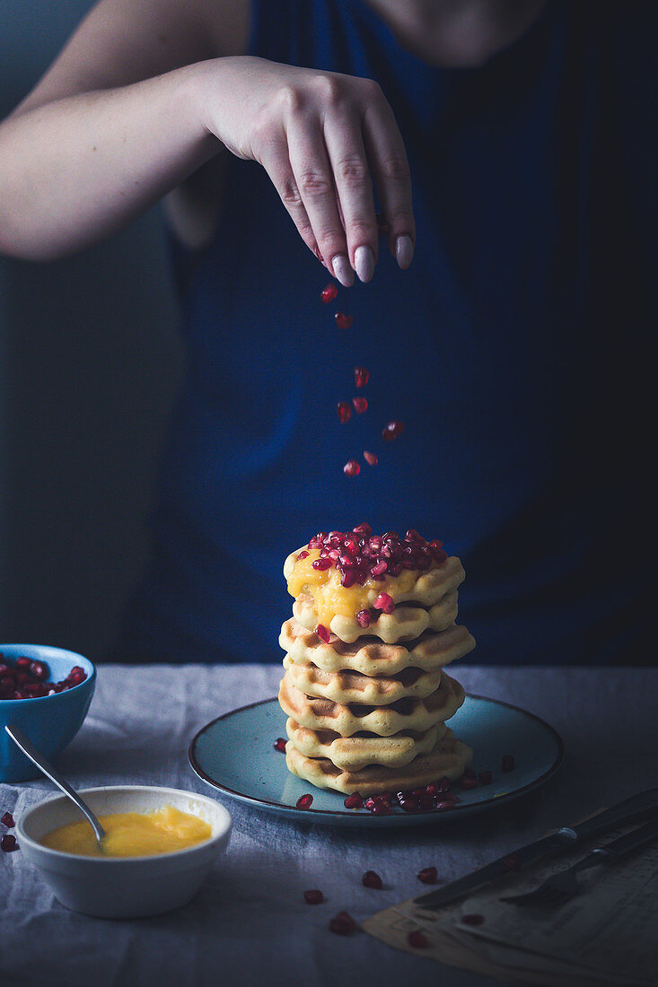 Woman sprinkling pomegranate seeds onto stack of waffles