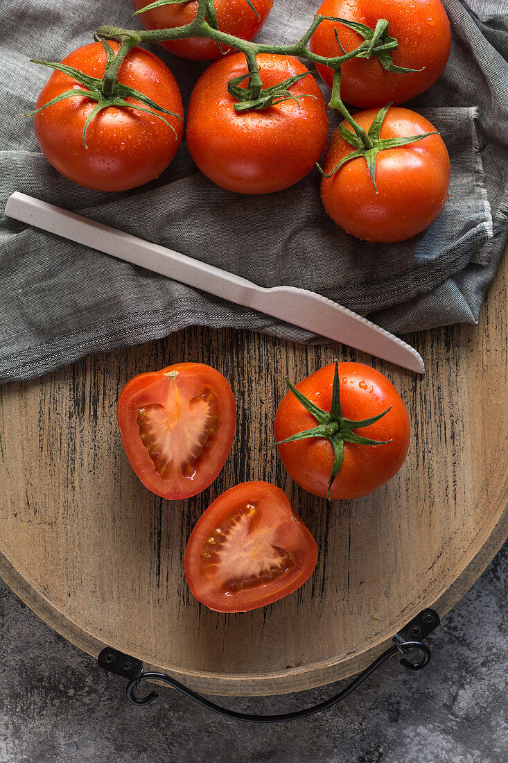 Halved and whole fresh tomatoes placed wooden board on rough gray table