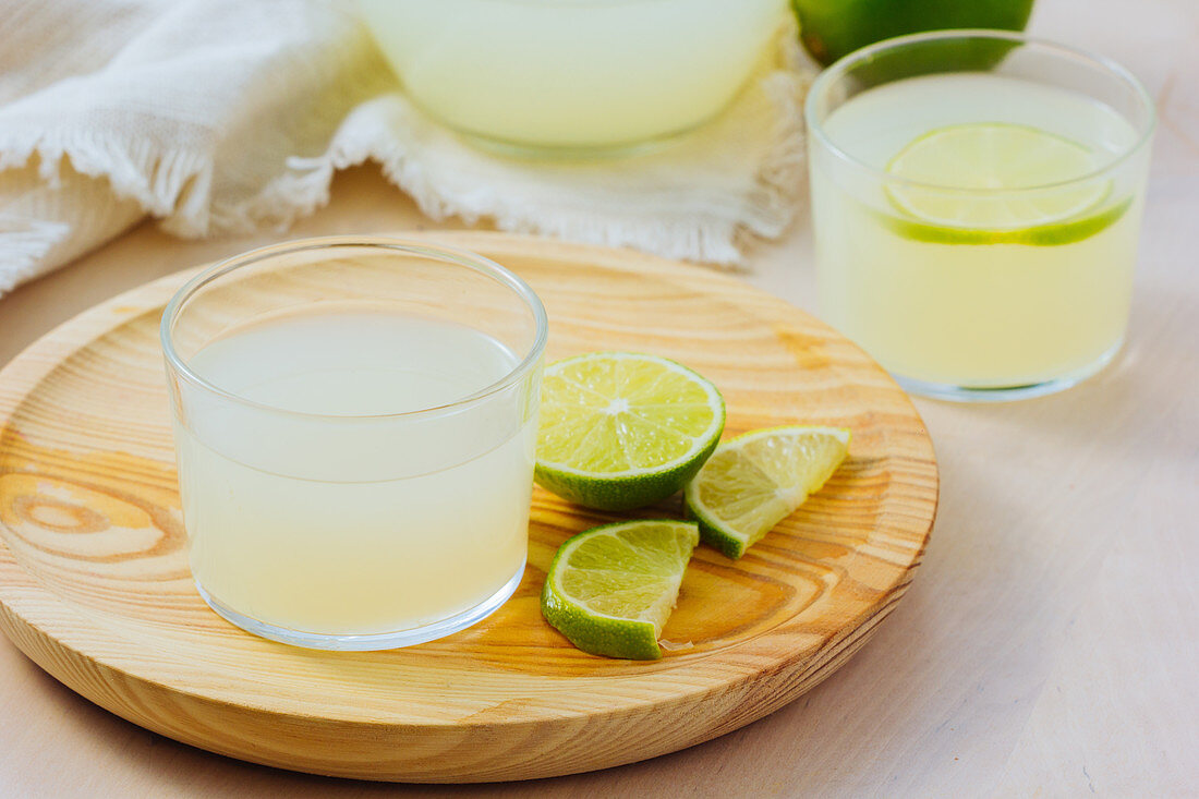 Homemade refreshing lemonade in server in glasses on wooden tray in white table background